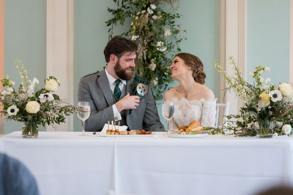 Wedding reception setup with romantic greenery and white floral decorations against a light-colored wall.