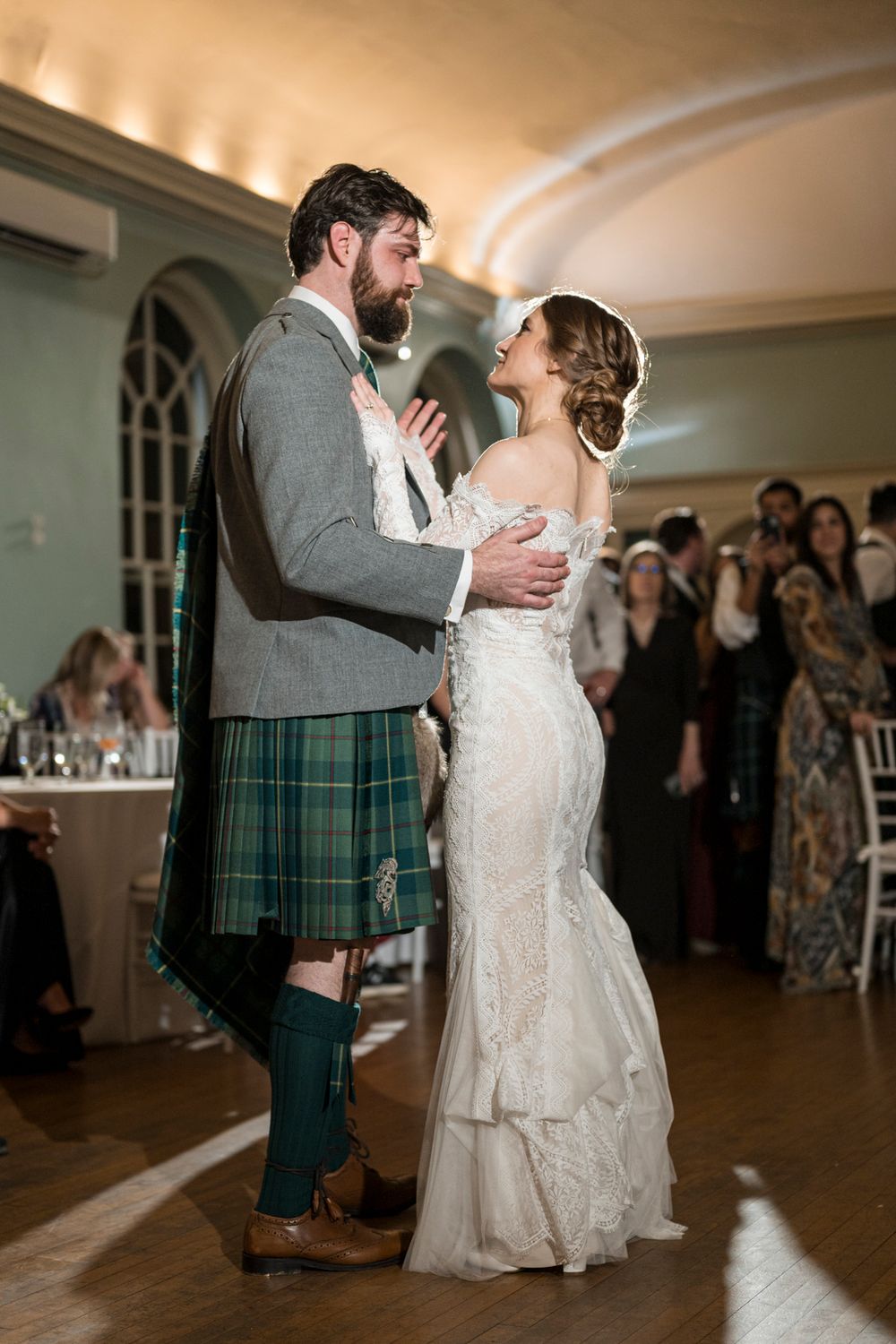 A couple shares their first dance at a Scottish wedding reception with the groom wearing a traditional kilt.