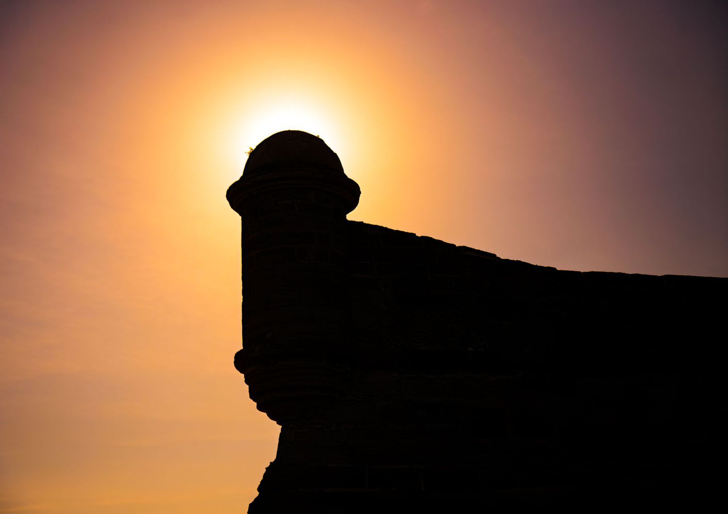 Silhouette of a stone watchtower at Castillo de San Marcos with the glowing sunset behind it in St. Augustine, Florida
