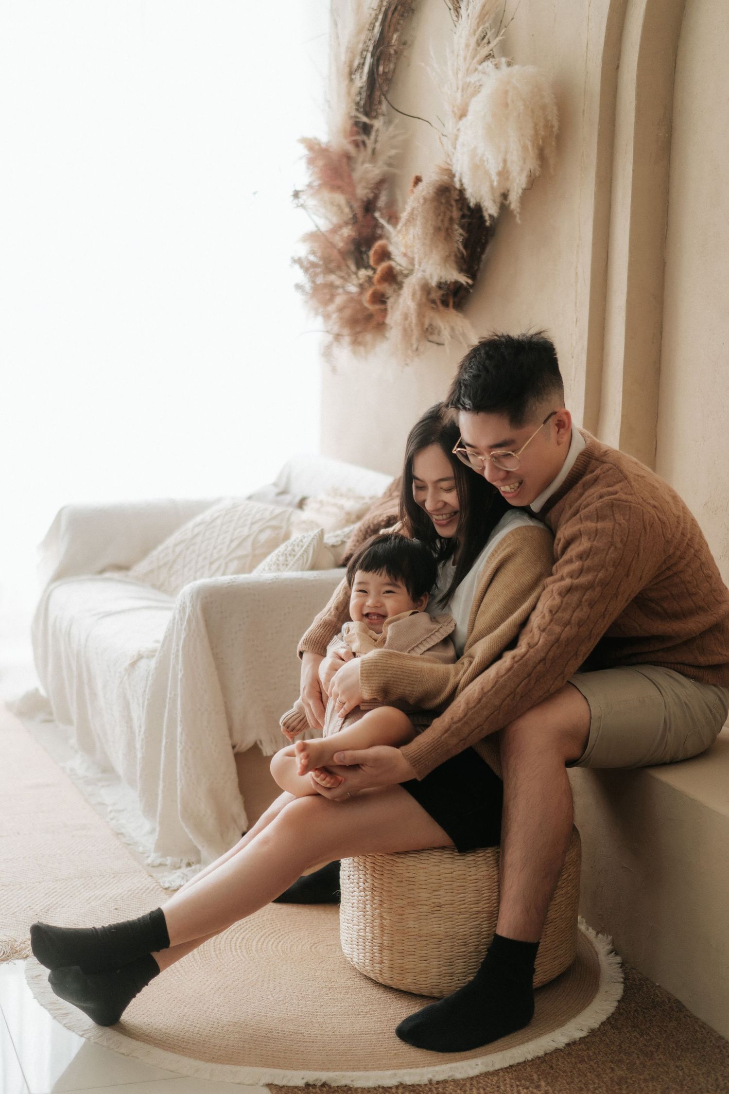 Family sits together on a white couch with pampas grass decor in a cozy minimalist setting一家人圍坐在白色沙發上，周圍環繞著蘆葦草裝飾，營造出溫馨簡約的氛圍。