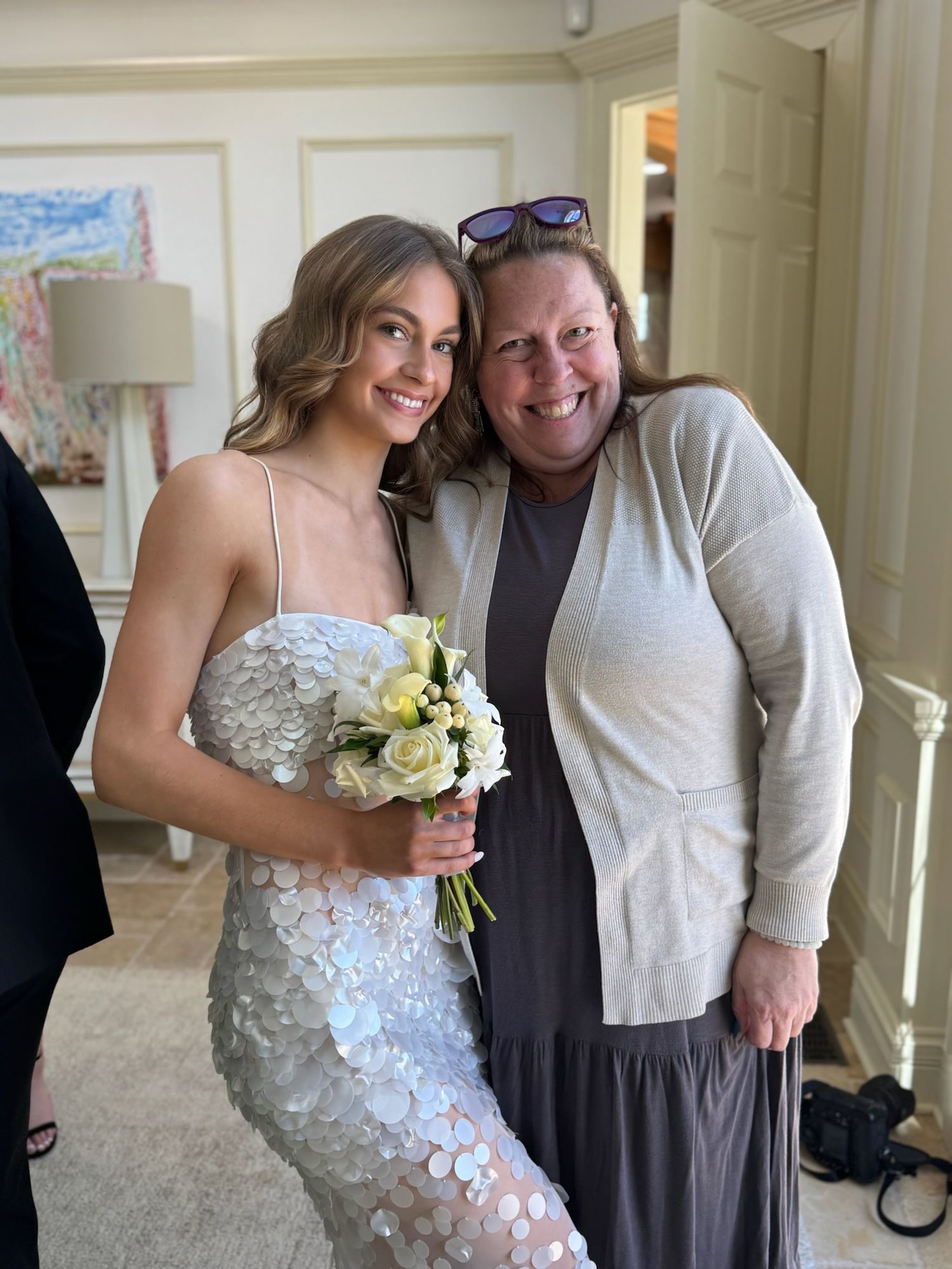 A bride in a white floral dress poses with guests in a formal interior setting.