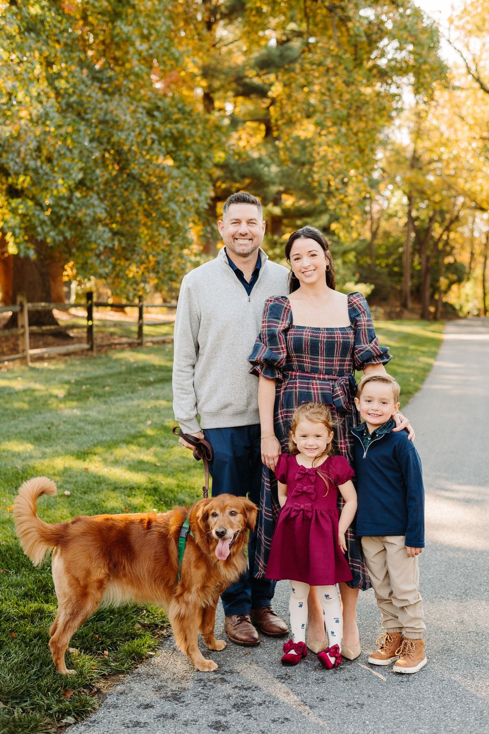 A family poses outdoors on an autumn path with their golden retriever dog during a fall photo session.