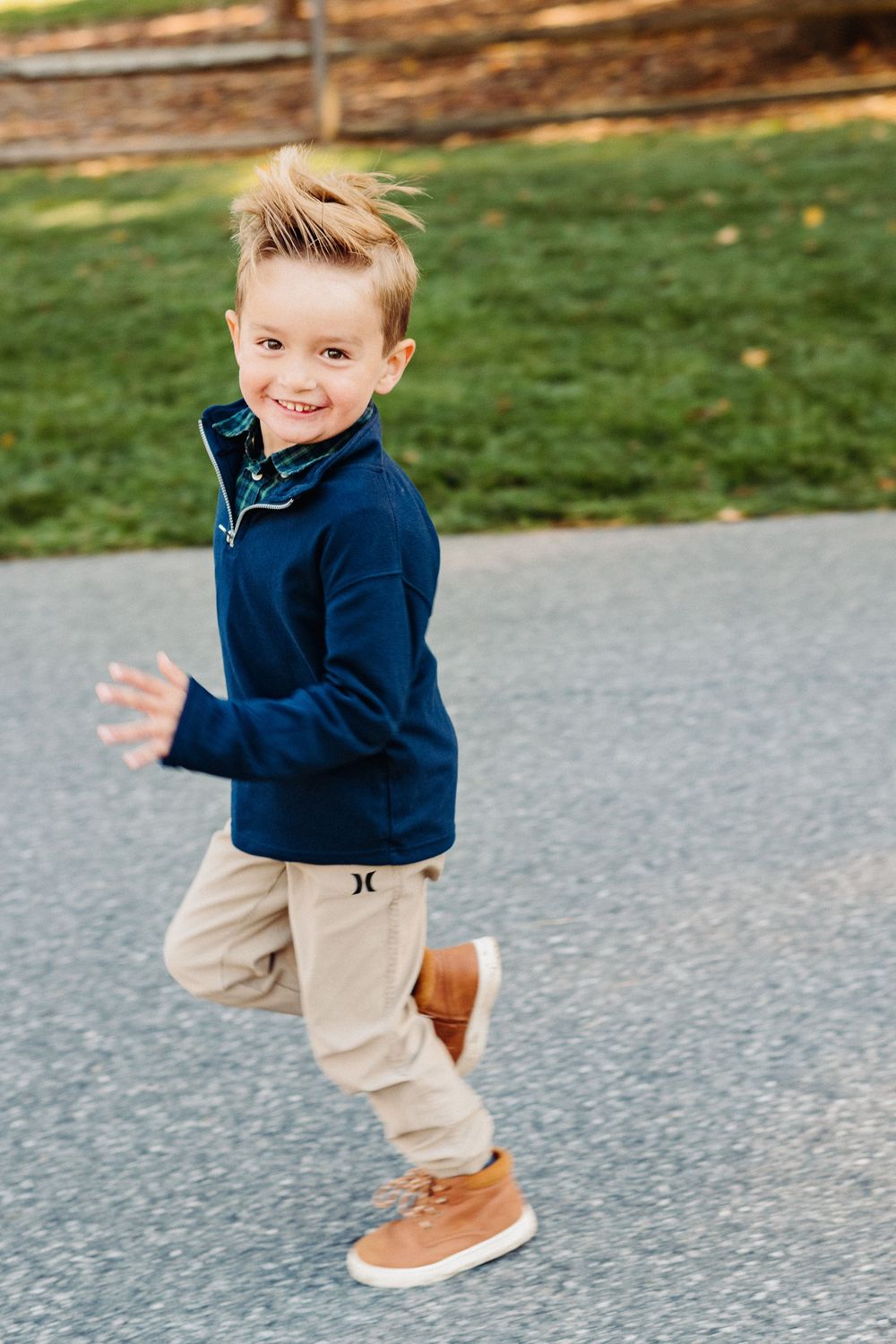Small child in navy sweater and khaki pants jumps playfully on a paved path during autumn.