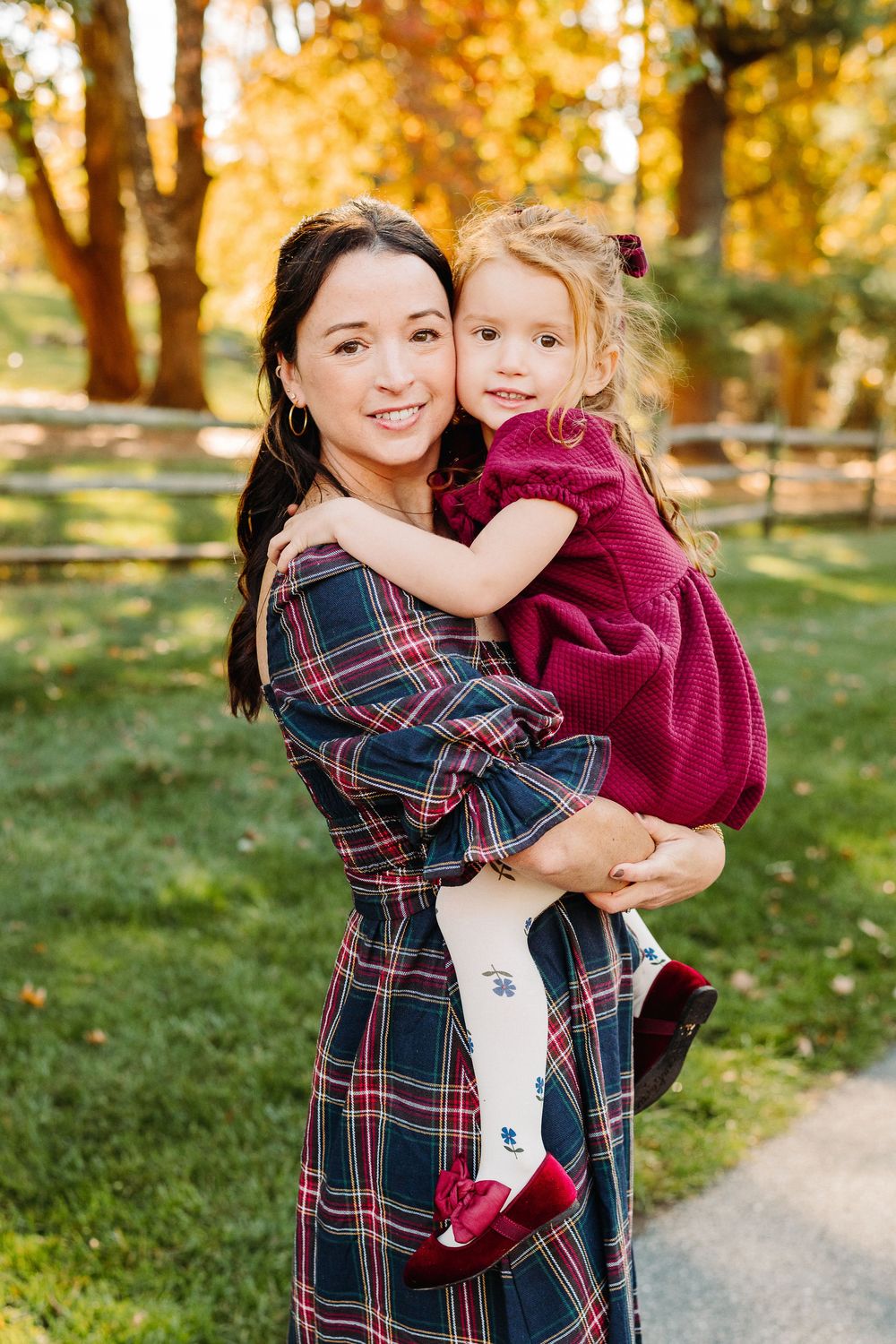 Two people hugging and smiling in a park with autumn foliage in the background.