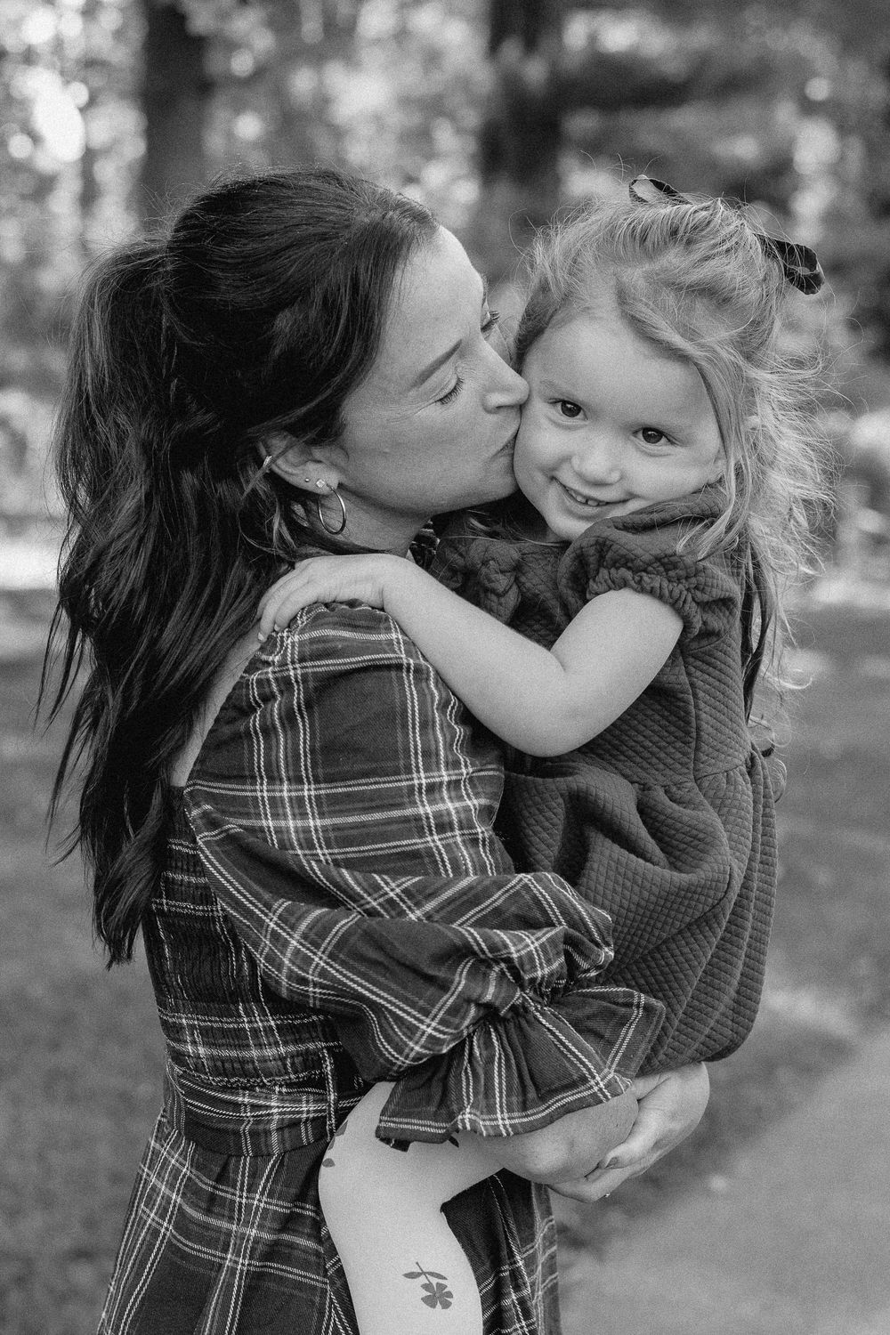 A series of black and white photos showing tender moments of affection and play between a parent and child outdoors.