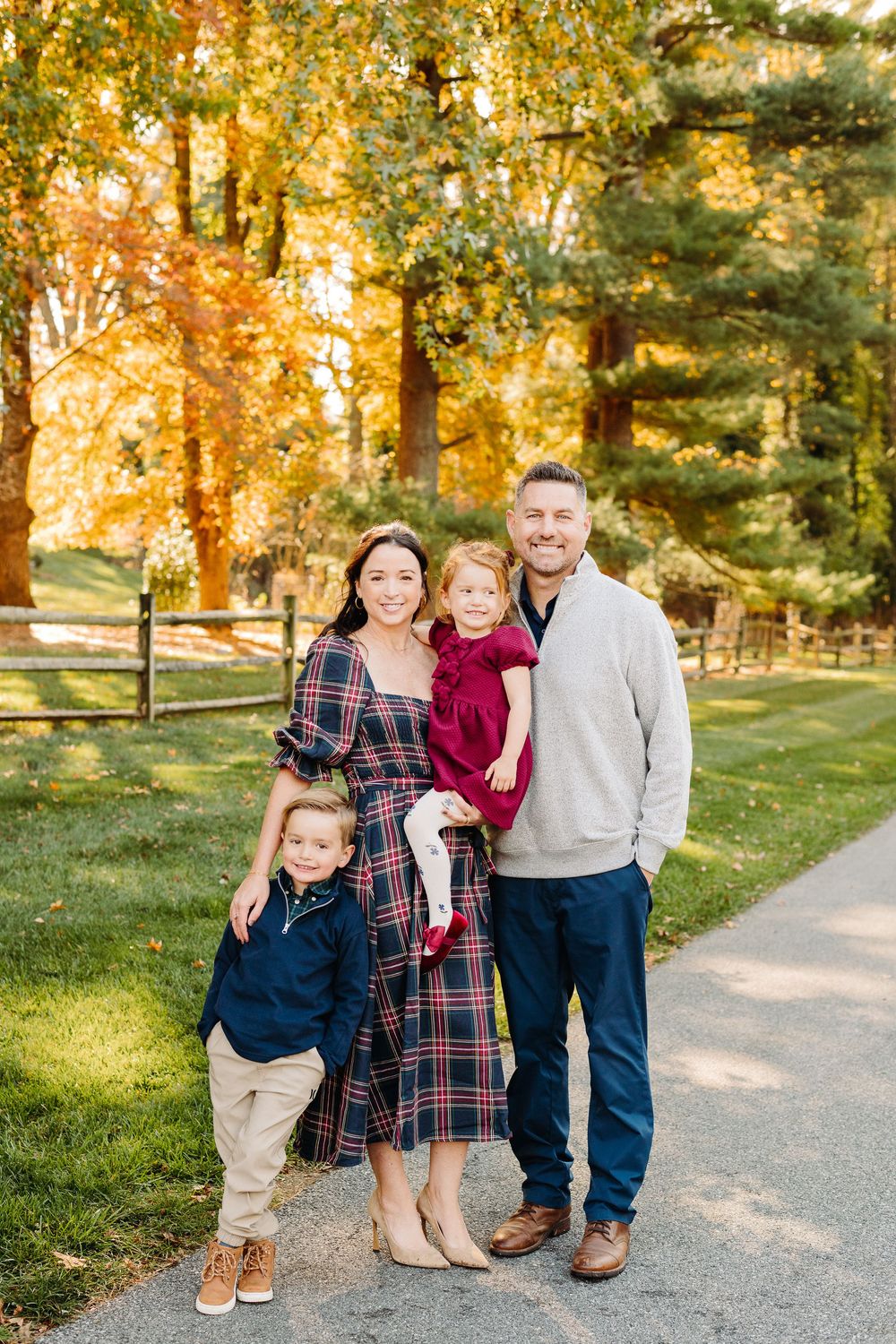 Family portrait session in a park with golden autumn foliage on a paved walking path.