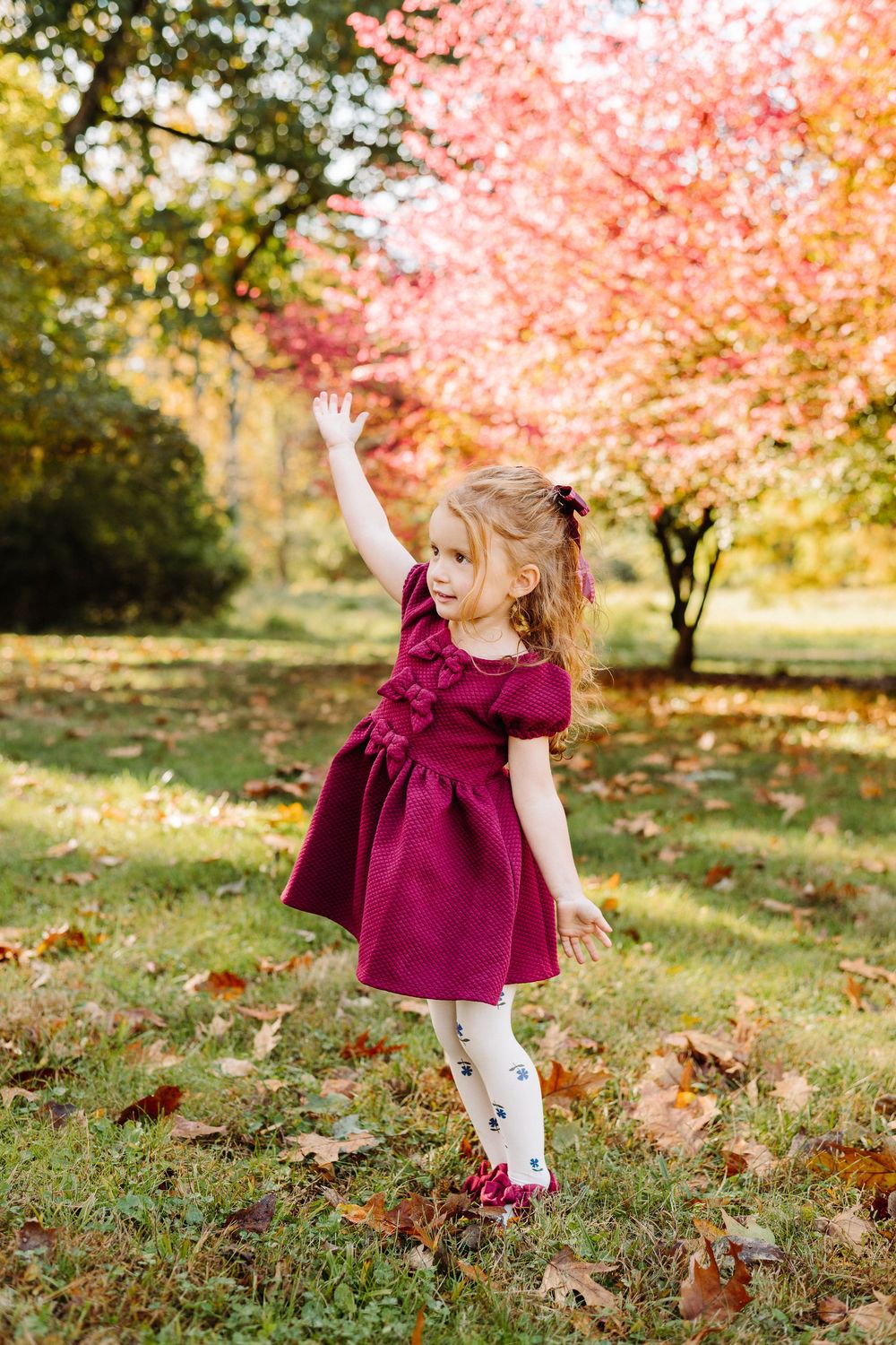 Young child in burgundy dress twirling and playing under pink cherry blossom trees.