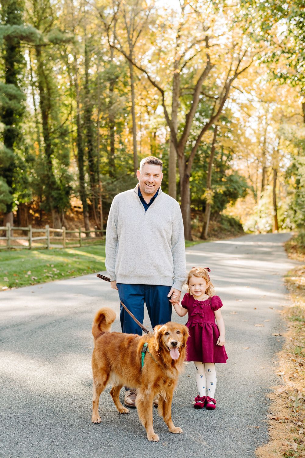 Family and golden retriever posing together on a tree-lined path during fall season.