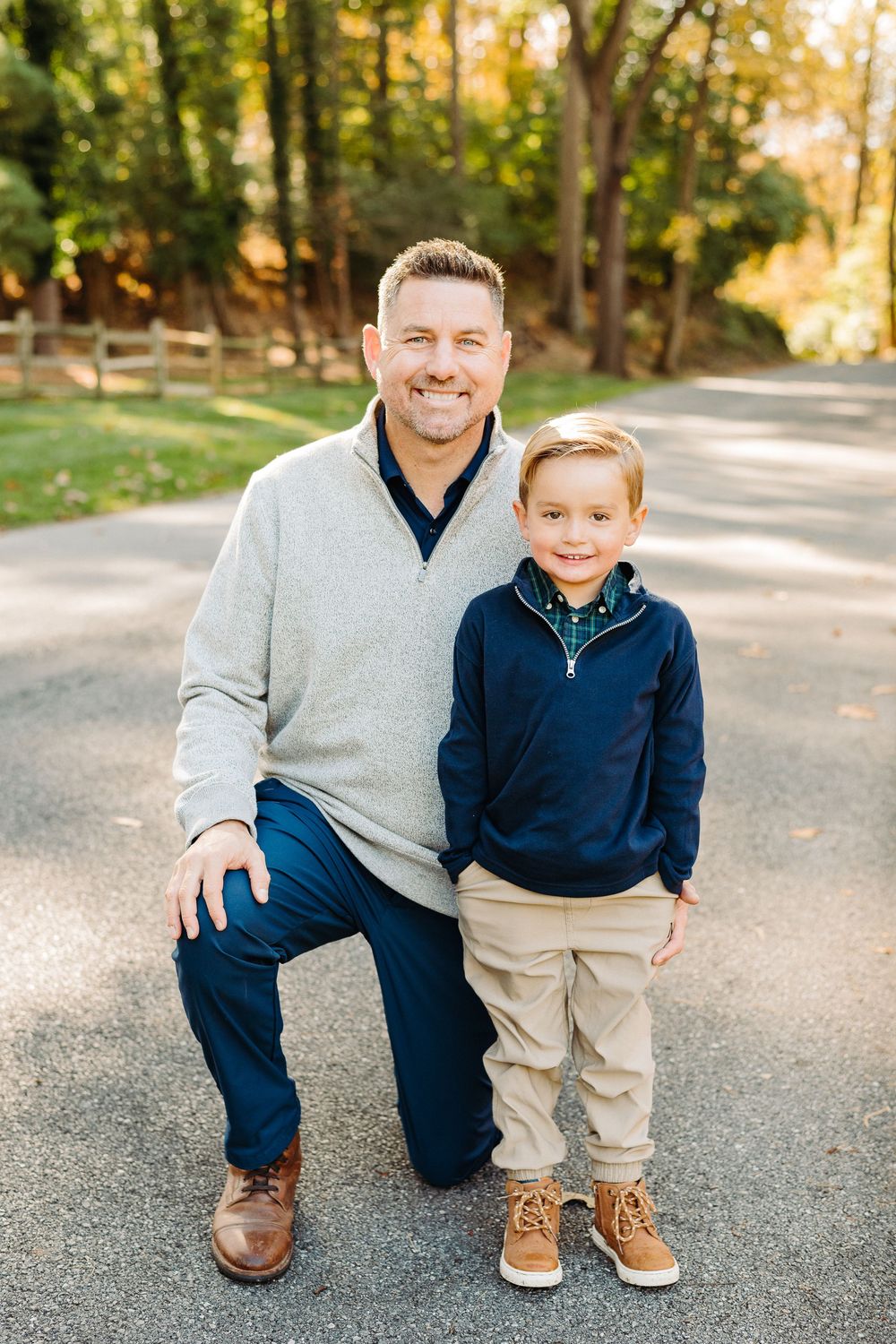 Father and son matching in navy blue outfits pose together on a gravel path during autumn.