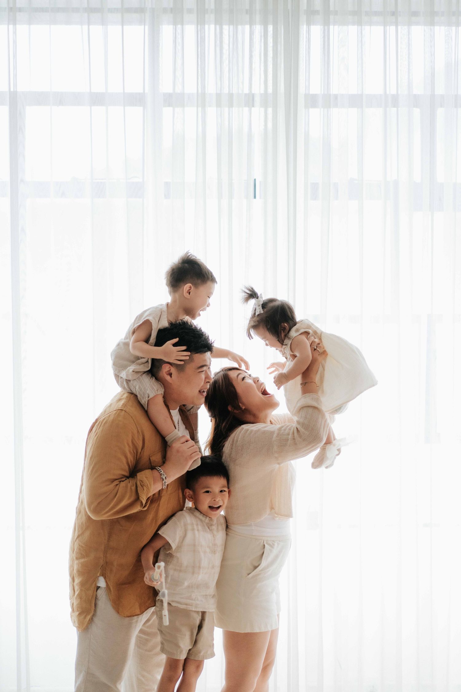 Happy Asian family with parents and three young children playing and laughing together in a bright, airy white room.幸福的亞洲家庭，父母和三個年幼的孩子在一個明亮通