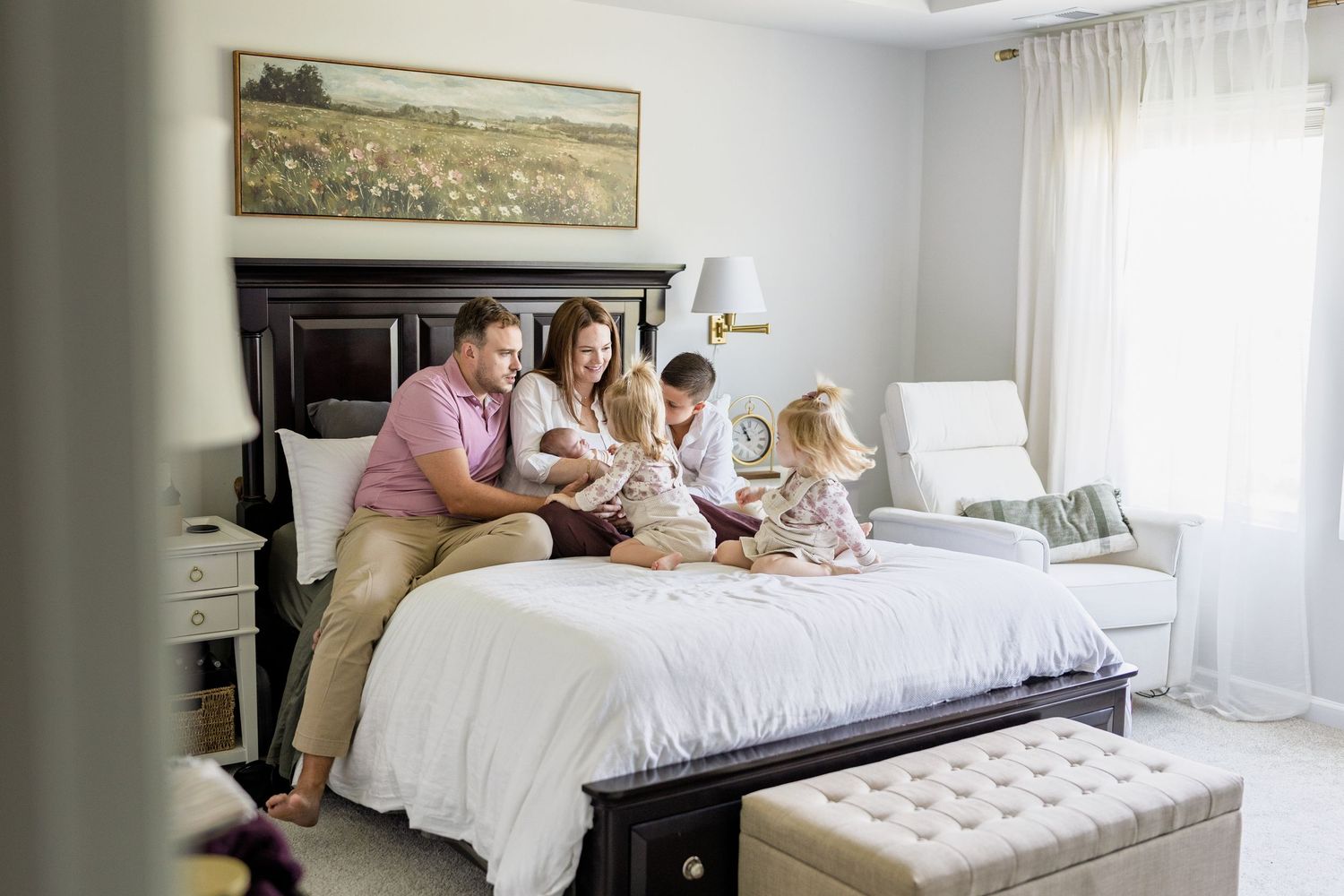 A bright and airy master bedroom features white bedding, sheer curtains, and a tufted bench at the foot of the bed.