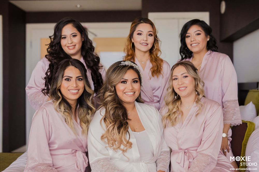 Bridal party in matching pink robes poses together with bride in white robe during wedding preparations.