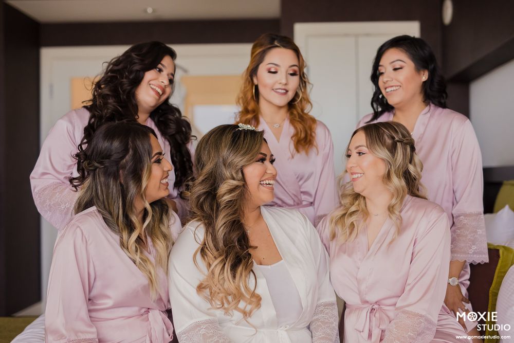 A group wearing matching pink robes poses together during wedding day preparations.
