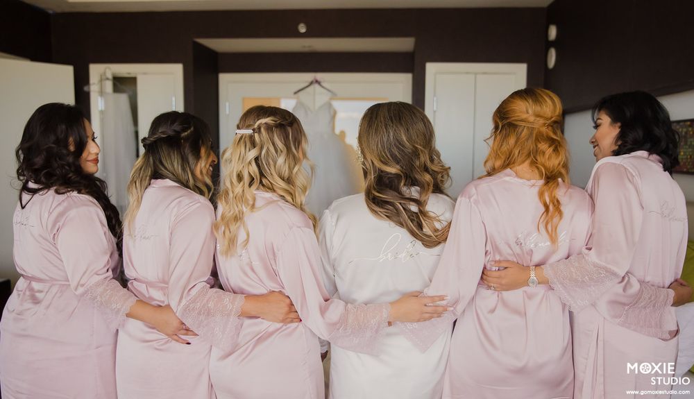 A line of bridesmaids in pink robes shown from behind as they stand together in a row.