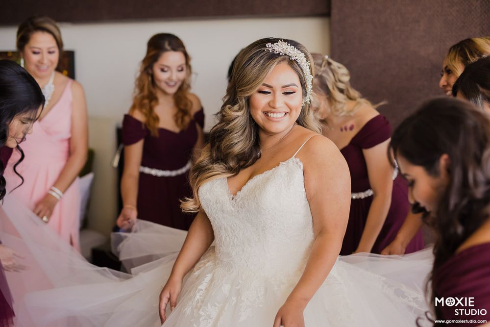 Wedding preparations scene showing bride in white dress with attendants helping get ready.