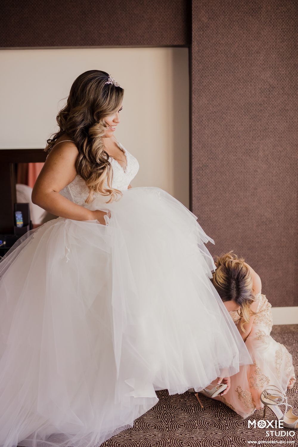 Helper adjusts the full tulle skirt of a wedding gown during final preparations.