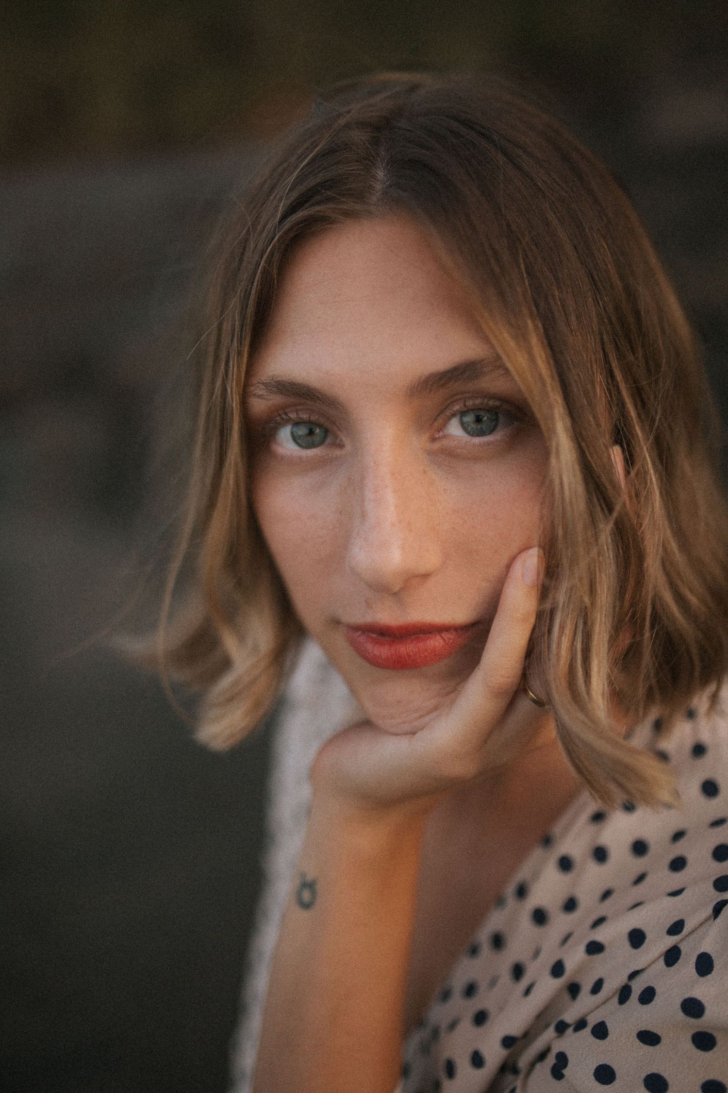 Close-up portrait of young woman with bob haircut resting chin on hand, wearing polka dot dress in New Zealand.