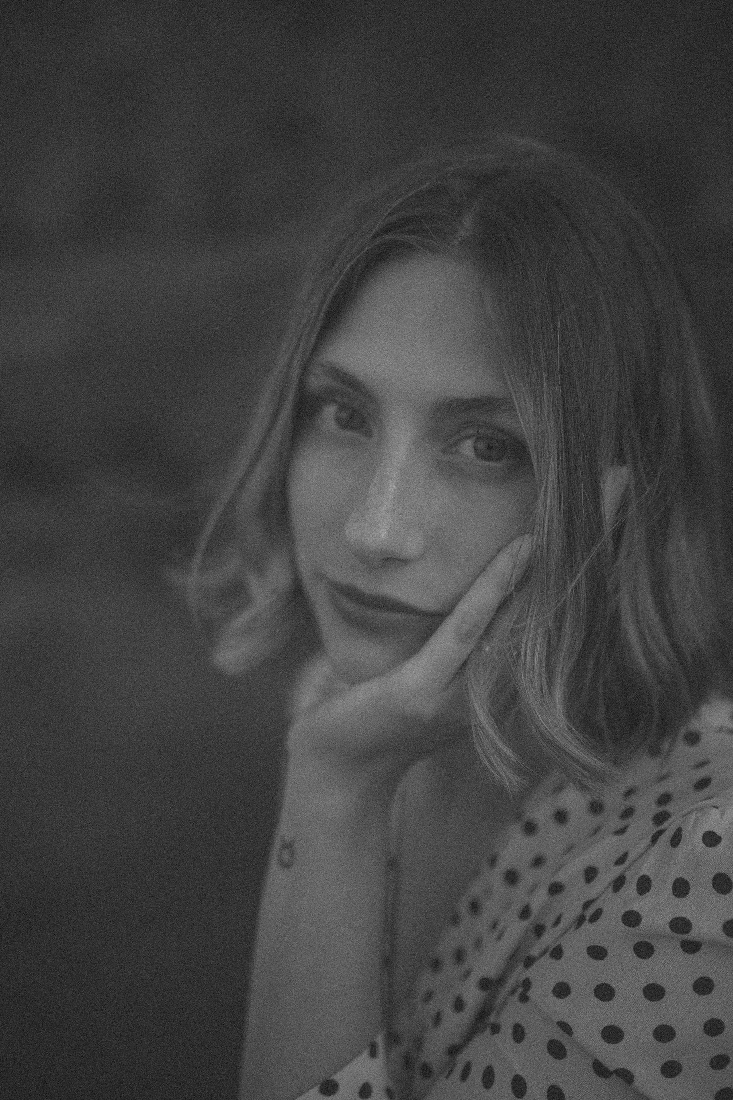 Black and white portrait of young woman with bob haircut resting hand on cheek, polka dot dress in New Zealand.