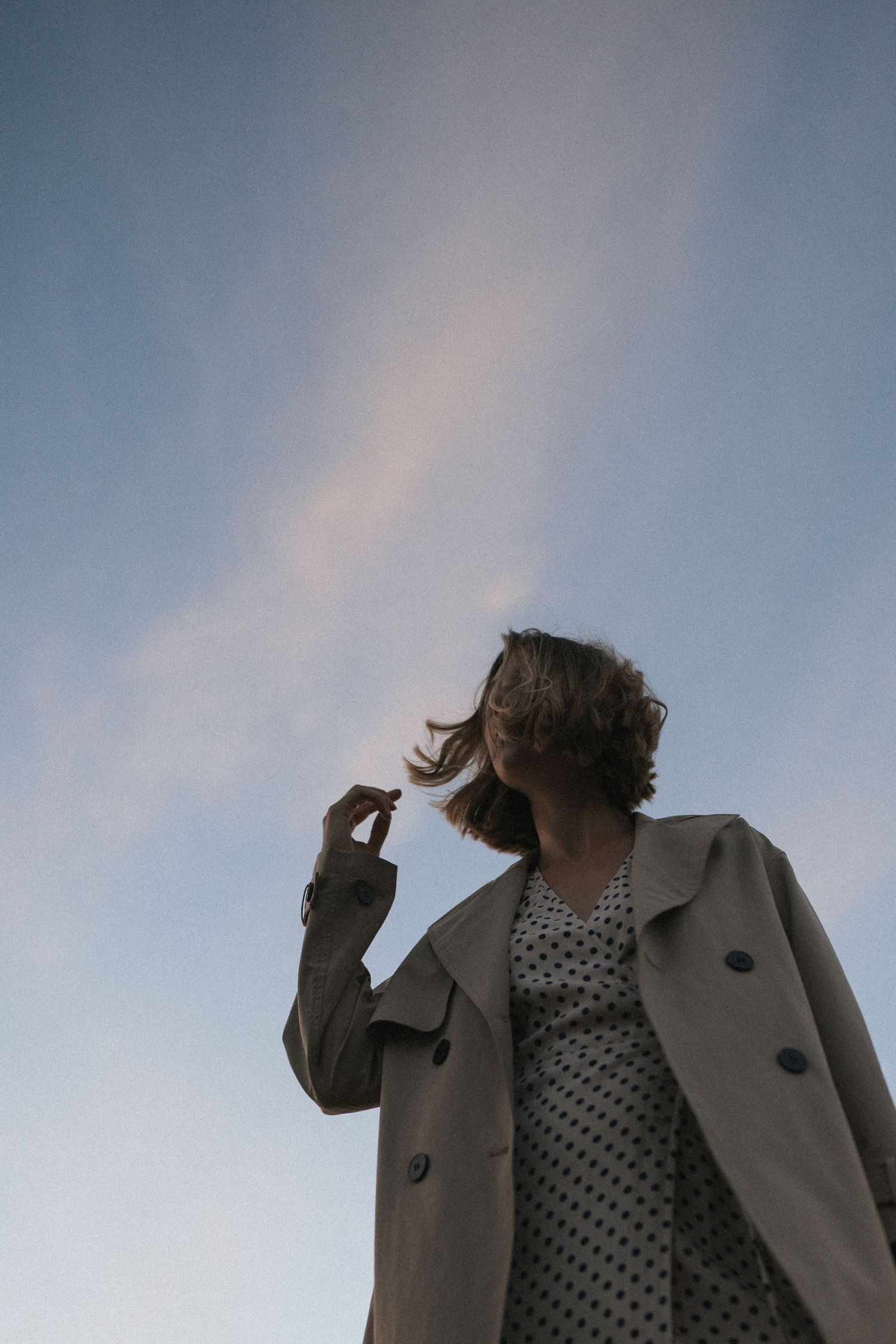Low angle view of woman in trench coat and polka dot dress against blue evening sky in New Zealand.