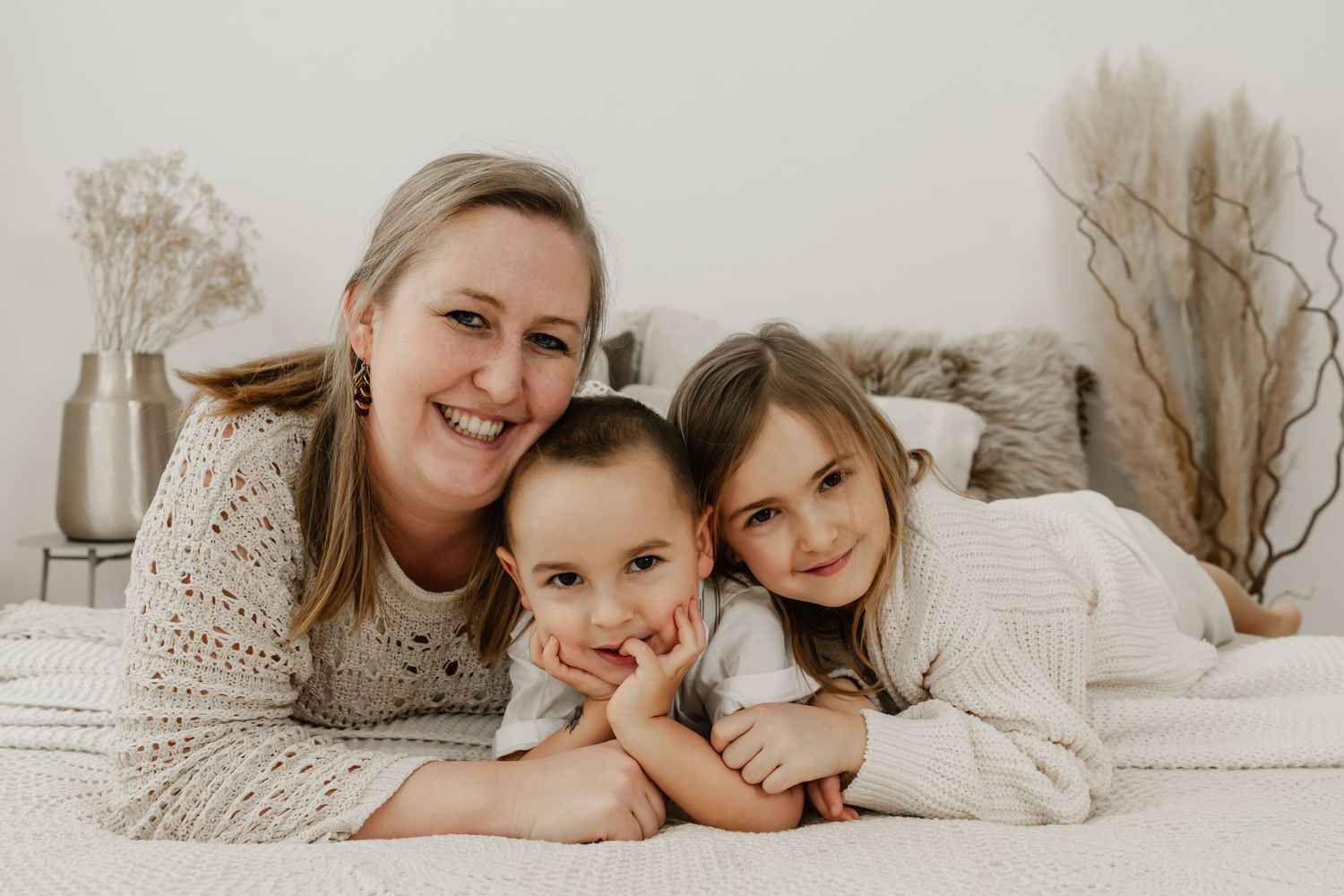 Mama, Sohn und Tochter liegen kuschelnd auf einem Shooting-Bett beim Familienfotoshooting im Fotostudio Stockerau und küssen den Sohn