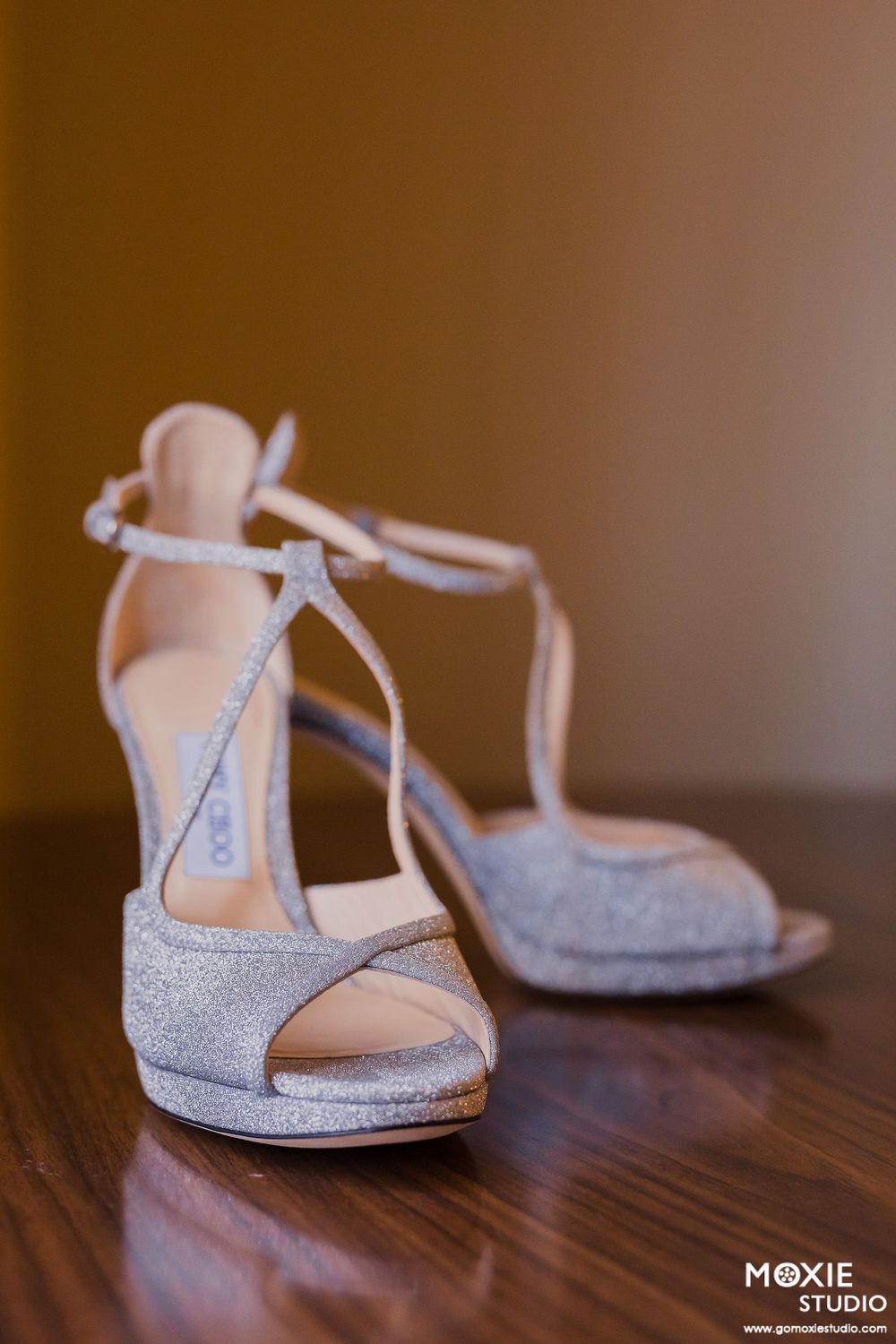 Silver glittery bridal shoes photographed on a dark wooden surface.