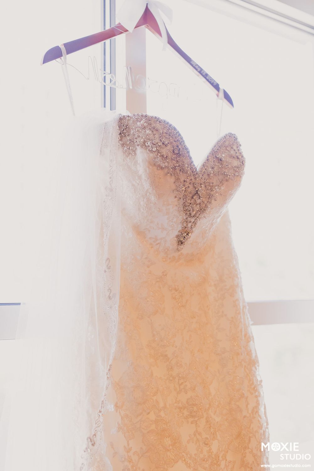 Elegant peach-colored wedding dress with lace details hanging on display against a white wall.