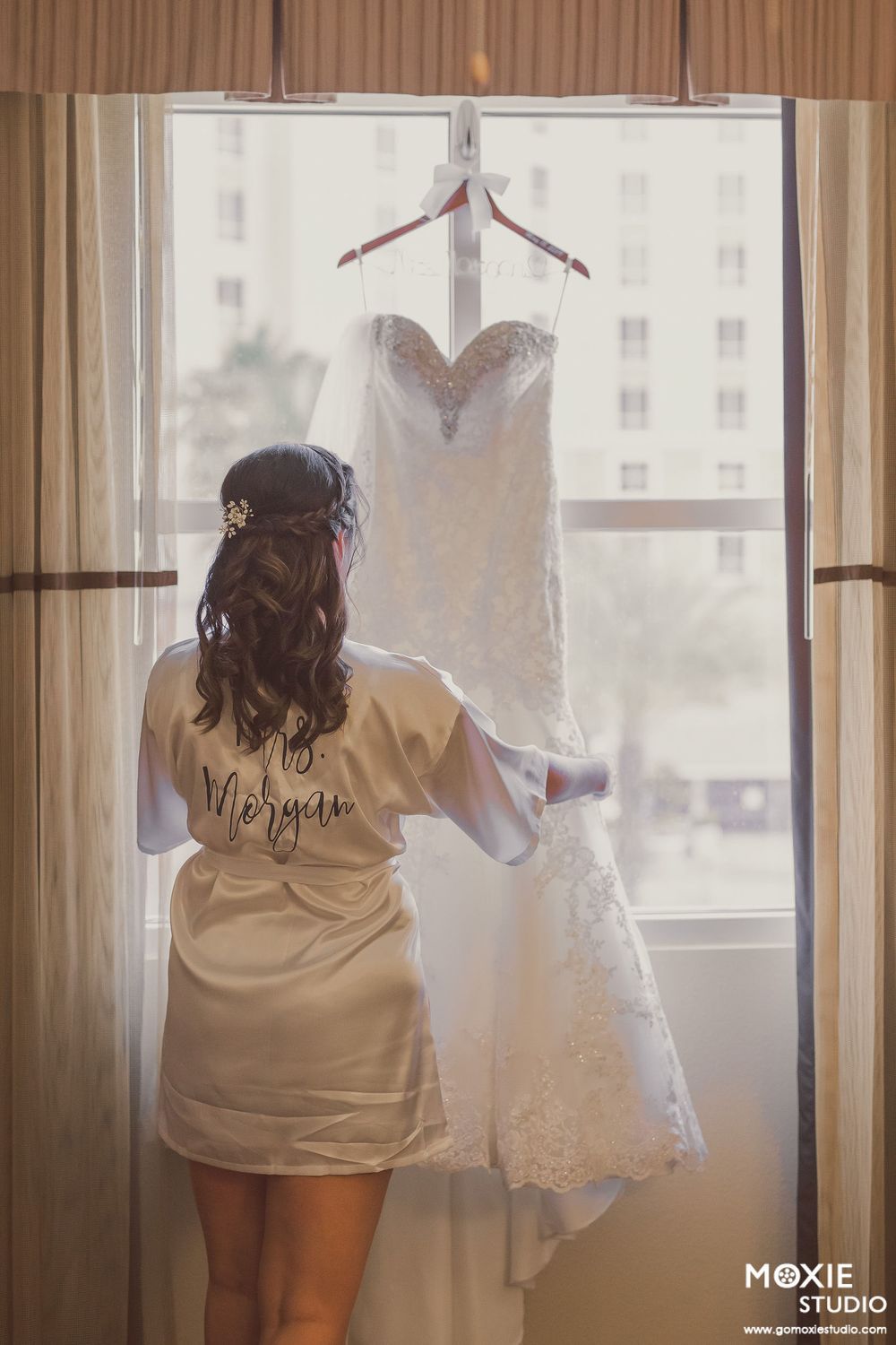 Wedding dress preparation scene with soft natural light streaming through curtained windows.