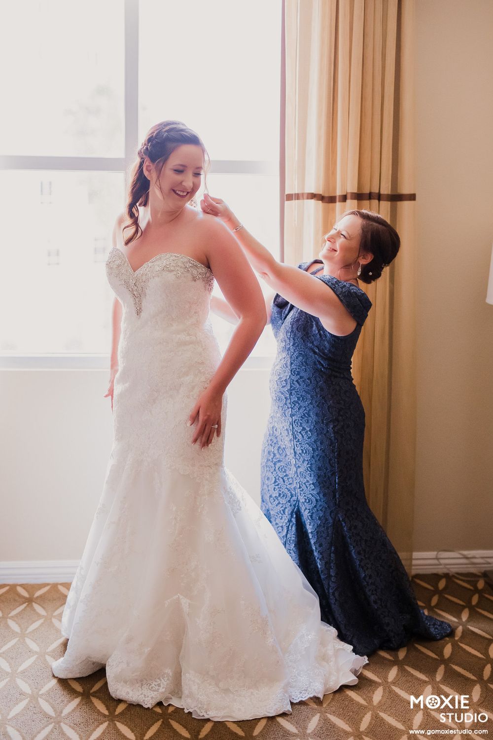 Final adjustments being made to a beautiful strapless wedding dress in a sunlit room.
