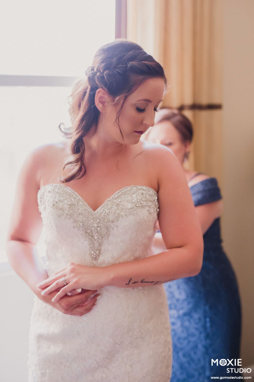 A bride in an elegant beaded strapless wedding gown looks down while getting ready before the ceremony.
