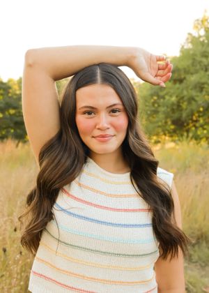 Casual portraits in a striped sweater tank top against a natural outdoor background.