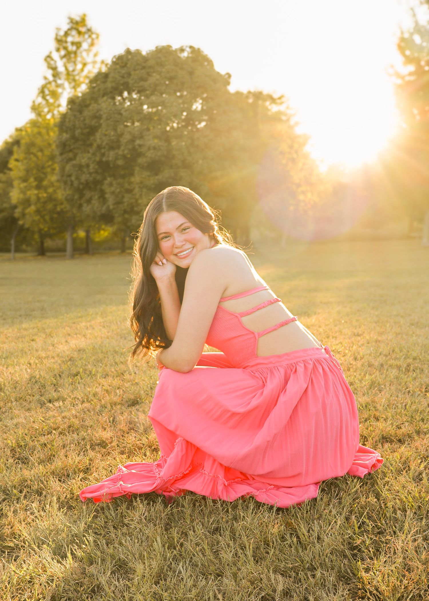 Dreamy sunset portraits in a coral pink dress laying in grassy field.