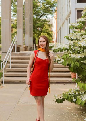 A person in a red dress stands by concrete stairs with flowering bushes in the background.