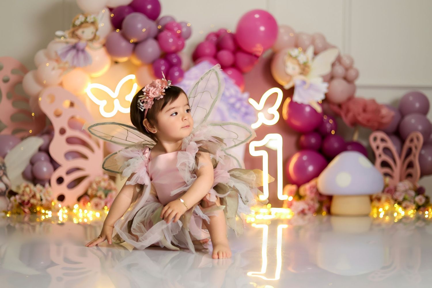 First birthday celebration setup with pink balloons, flowers, and glowing number one sign.