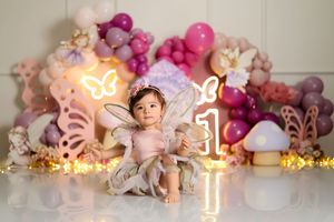 Whimsical birthday photo setup with pink and purple balloon arch and neon lighting.