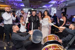 Musicians perform traditional Middle Eastern music with drums and percussion at a wedding reception with purple lighting.