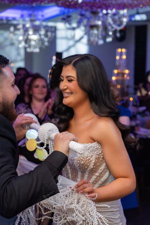 A person in a sparkly strapless gown smiles and holds a drink at an evening event.