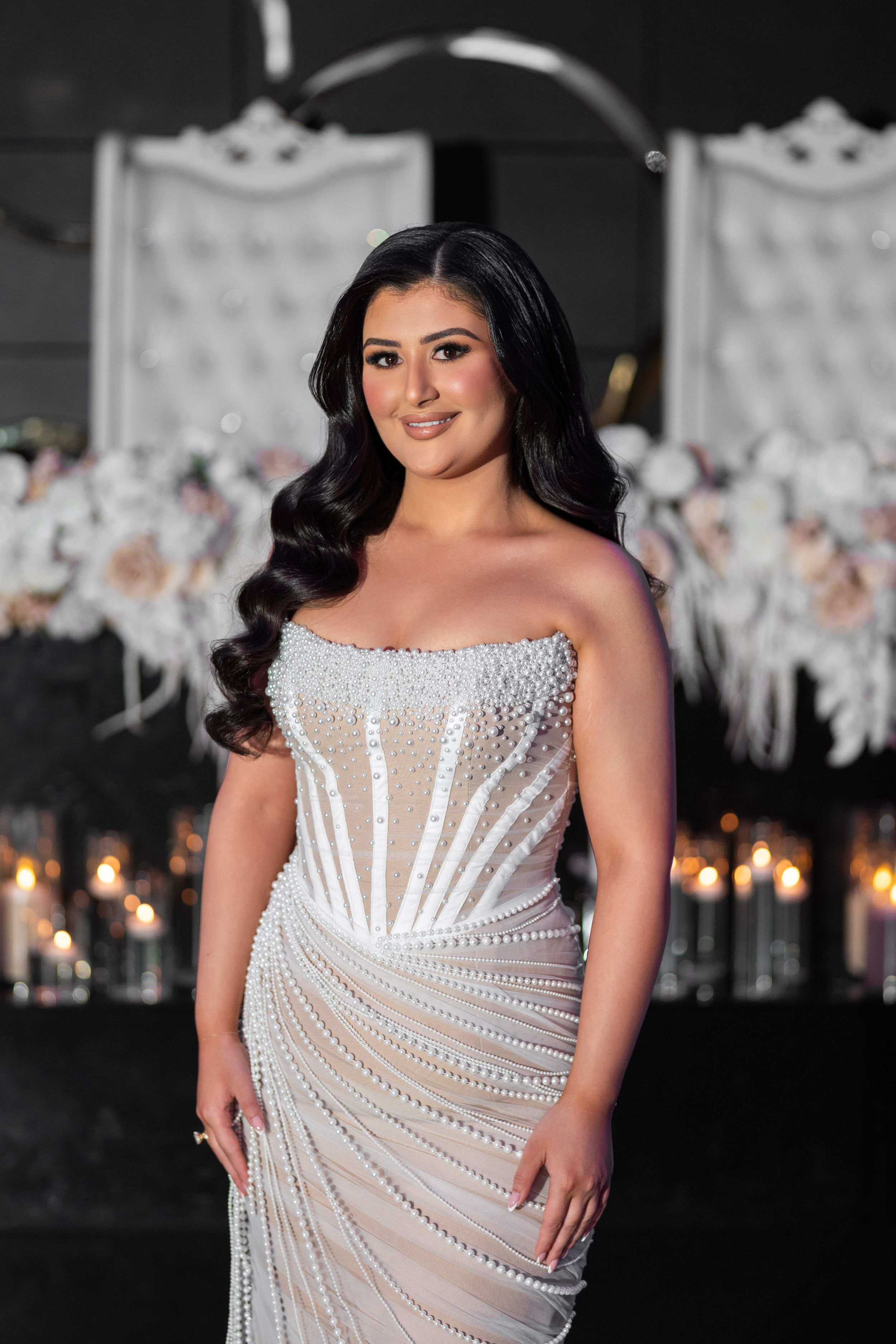 A stunning beaded white wedding gown with corset bodice and sweeping crystal details in an elegant venue with candles.