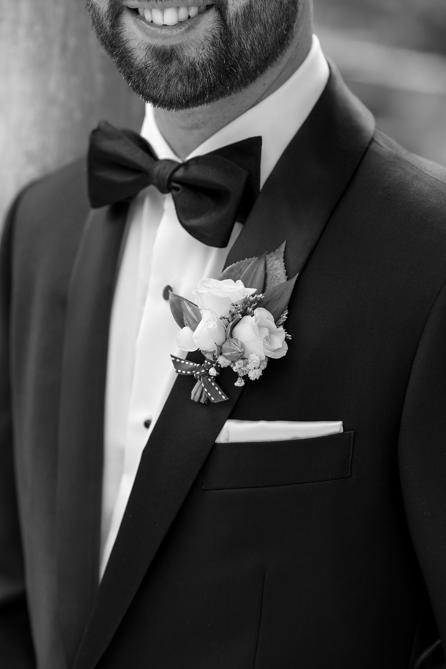 Close-up black and white photo of formal tuxedo with bow tie and white floral boutonniere on lapel.