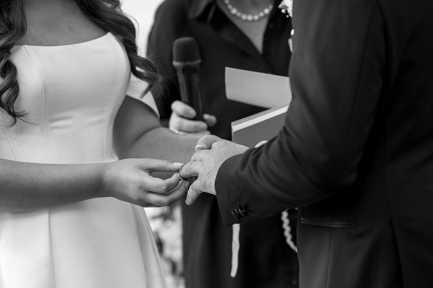 Black and white close-up of hands exchanging rings during a wedding ceremony with white dress visible at Browns Brothers Winery.