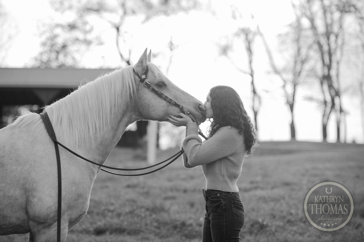 Black and white photo of person and horse sharing intimate moment in pasture.