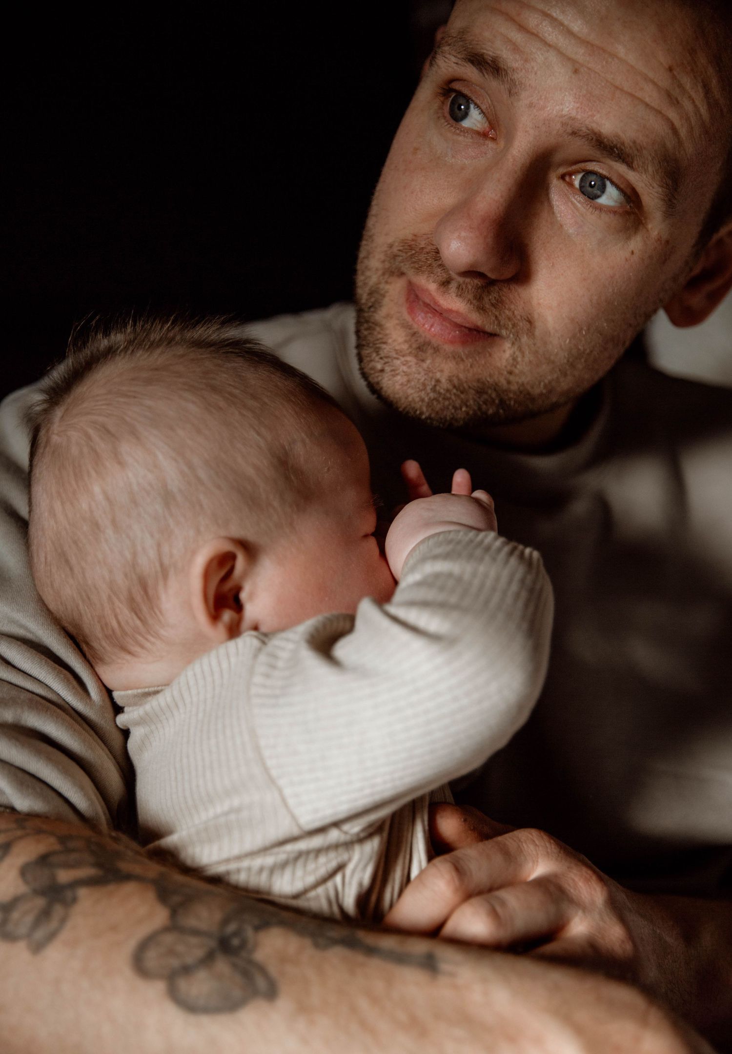 Intimate bonding moment between parent with tattoos and sleeping infant.