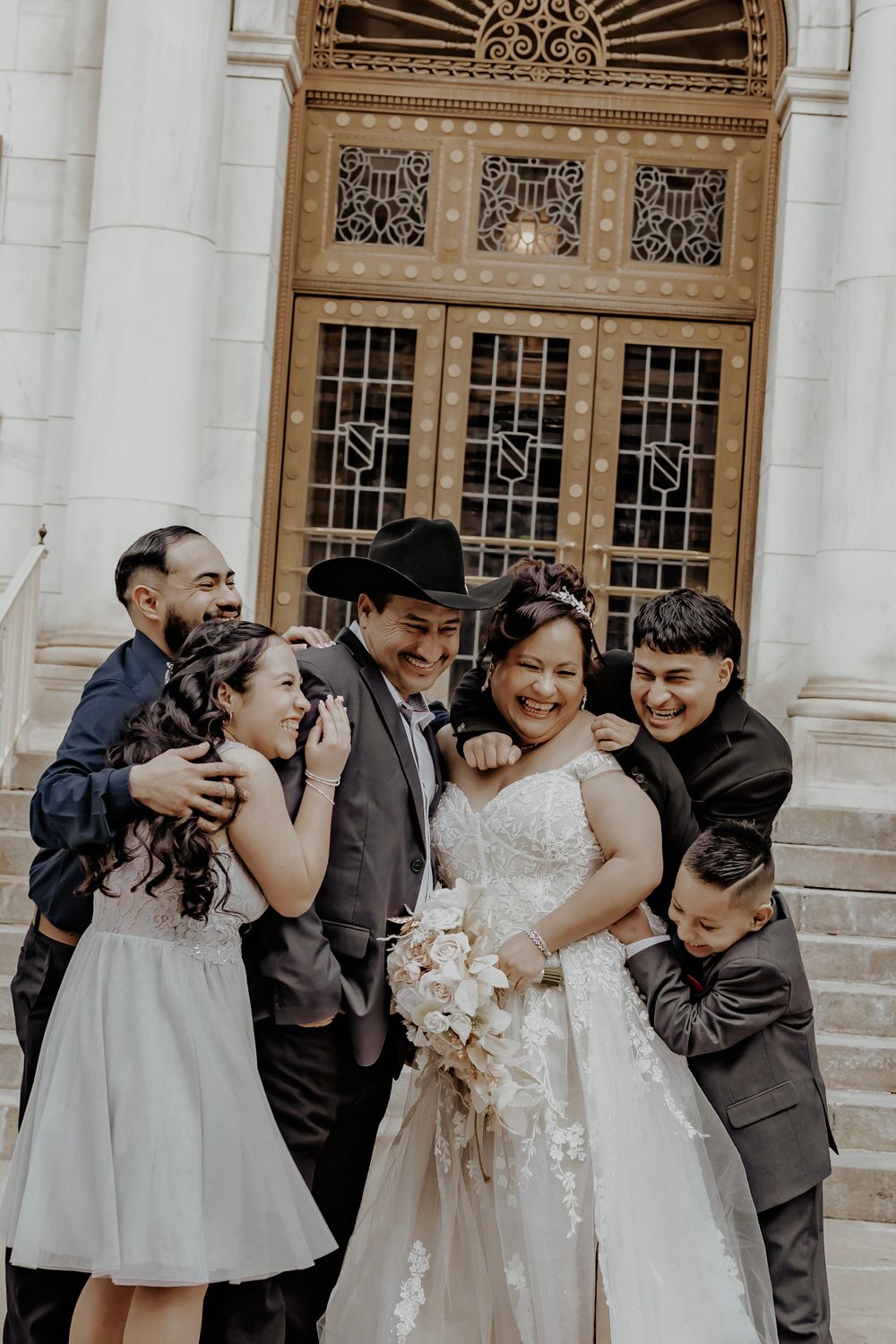 Bride and groom with their family laughing in front of a building
