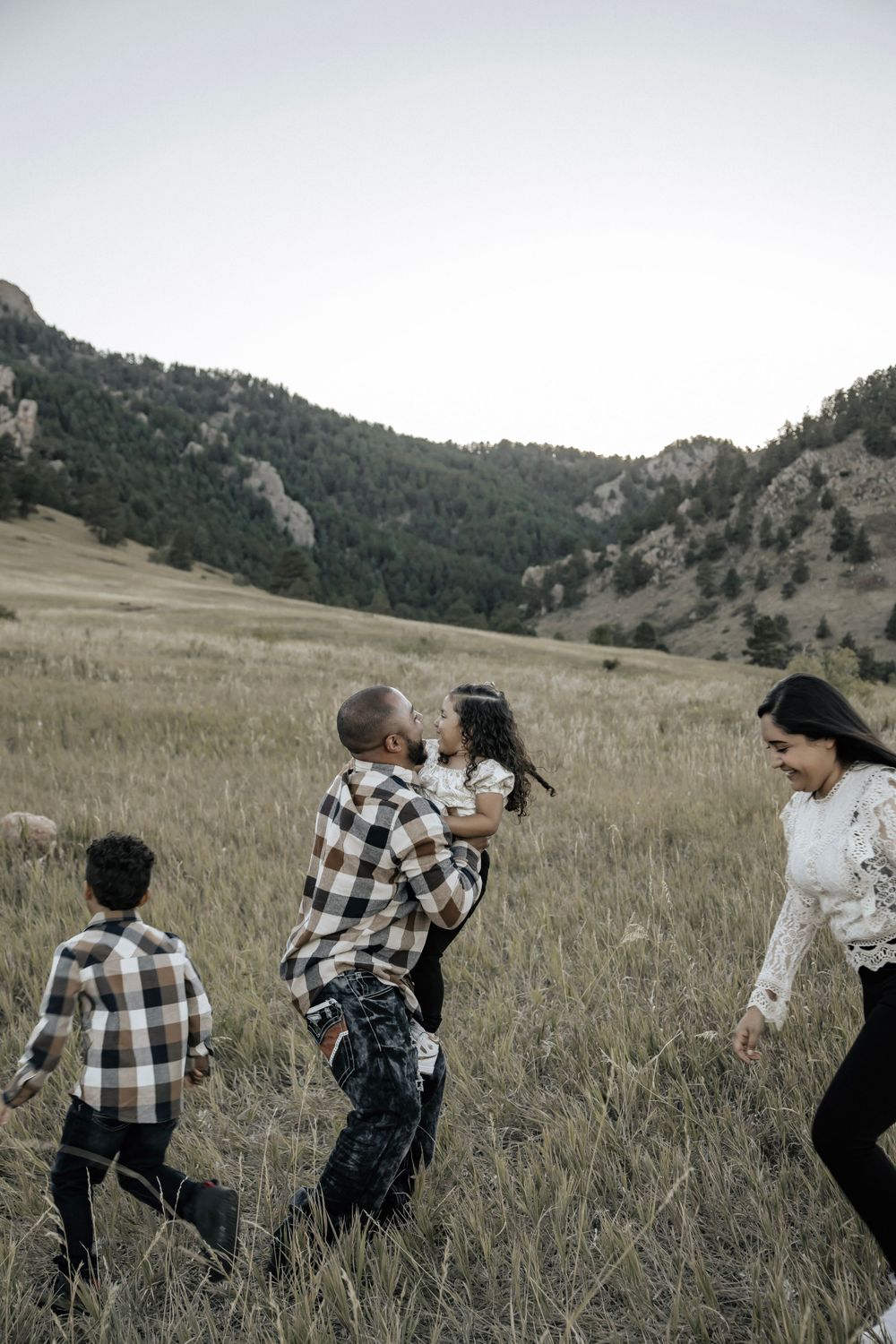 Dad hugging daughter while mom and son run around in a field with mountain in the background