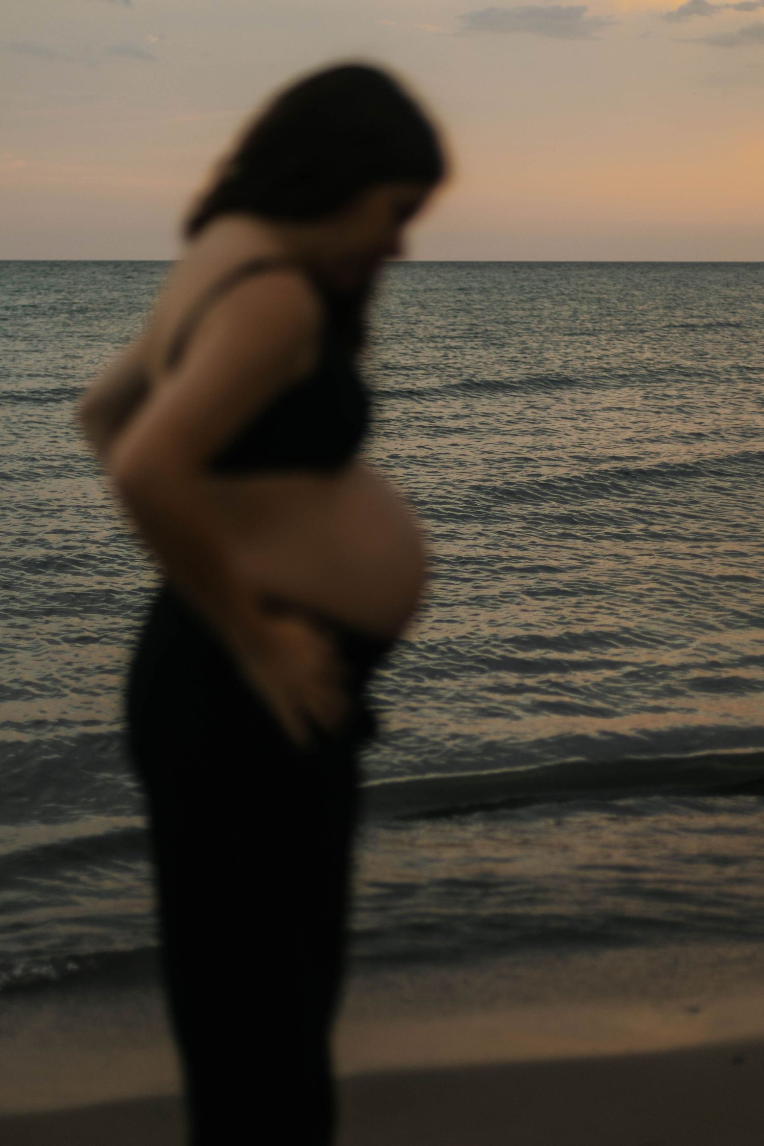 pregnant woman and looking at ther belly while the sun gets down, on the side of the lake, at the Bluffs in Scarborough, Toronto