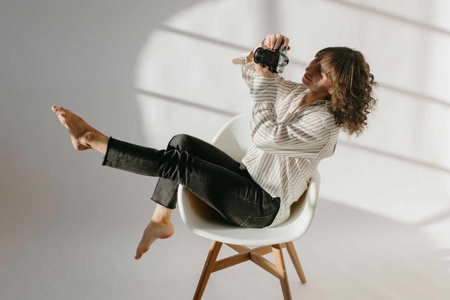 professional event photographer sitting in a chair in a studio with white background behind her, holding up a camera and looking at it