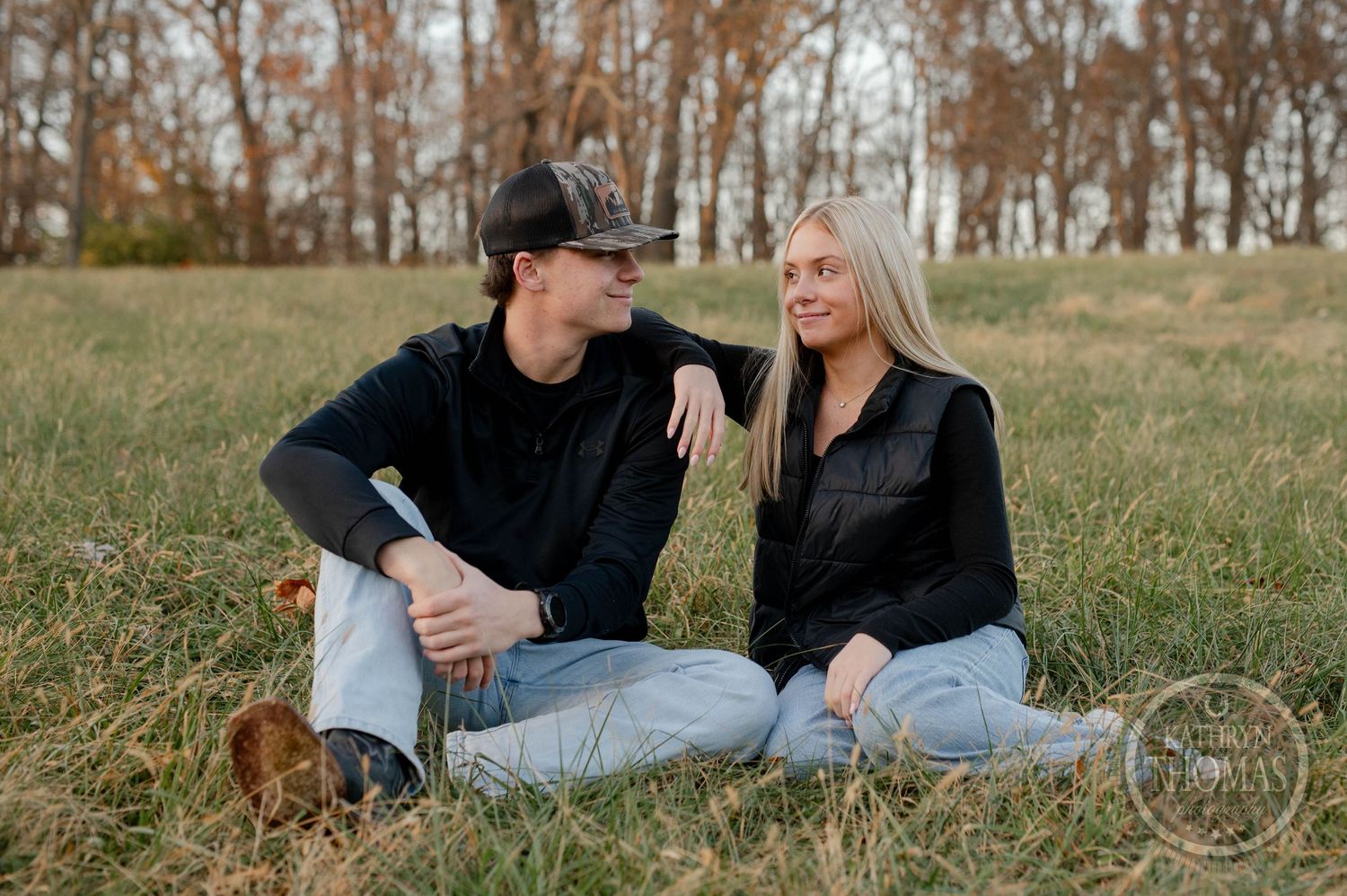 Casual outdoor portrait of siblings sitting in grass with autumn trees .