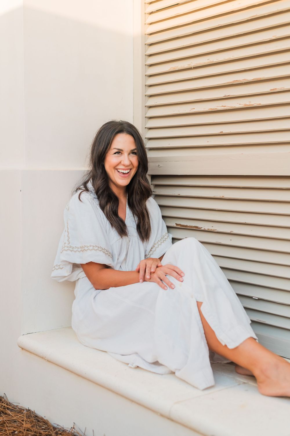 Casual outdoor portrait of person sitting on white ledge wearing light blue and white lace-trimmed dress.