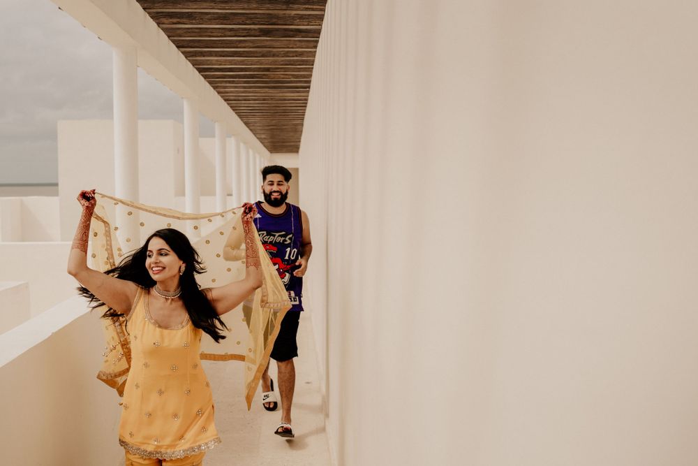 A couple poses playfully in a hallway, with one walking behind as the other dances in a yellow dress.