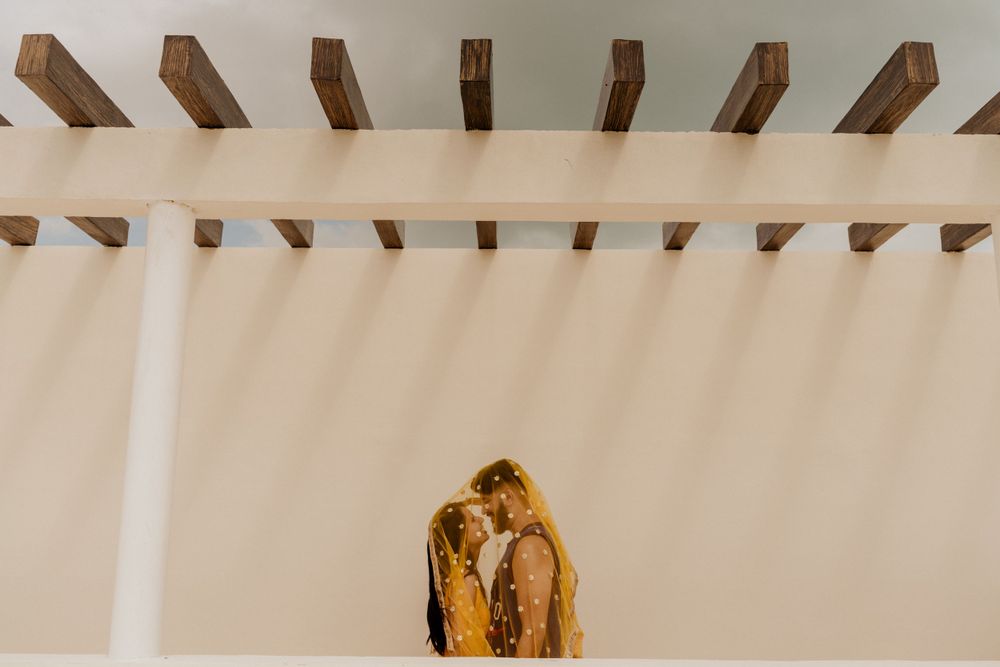 A couple standing close together under a modern white pergola with wooden beams overhead.
