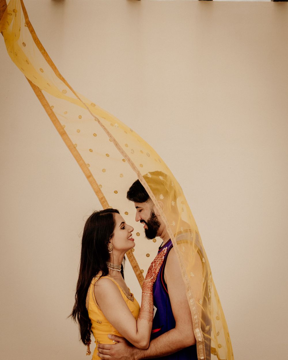 Romantic couple poses with flowing yellow fabric against beige wall as their silhouettes create artistic composition.